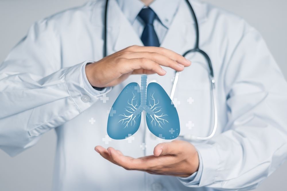 Un medico in camice con un'illustrazione dell'apparato respiratorio fra le mani